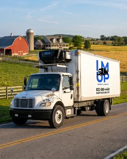 An IM UP Trucking commercial semi-truck parked near a farm field representing agricultural logistics